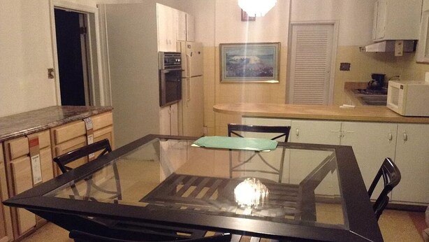A compact kitchen with a glass-top dining table, white cabinets, and basic appliances. - Single family home+ large rooms +kitchen + living room+den roo + beautiful  yard (Catonsville)