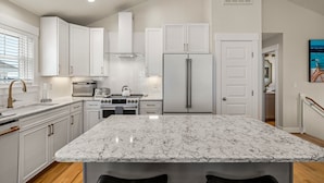 A modern kitchen with white cabinetry, a marble island, stainless steel appliances, and a herringbone tile backsplash. - Close to beach, on golf course in TCC!  Private pool, spa, and 6 seat golf cart! (Corolla)