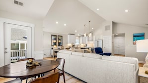 A modern kitchen with white cabinets, a dining area with a round table and chairs, and a large L-shaped sofa. - Close to beach, on golf course in TCC!  Private pool, spa, and 6 seat golf cart! (Corolla)