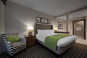 A hotel room with a large bed, a chair, two bedside tables with lamps, and framed pictures on the wall.