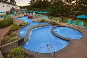 A swimming pool area with multiple pools, lounge chairs, and umbrellas.