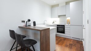 A modern kitchen with white cabinets, a wooden island, two black chairs, and a built-in oven. - Fernbank by Dublin At Home (Dublin)