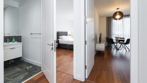 A modern hotel room with a bathroom, a bed, a dining area, and a view of the city. - Fernbank by Dublin At Home (Dublin)