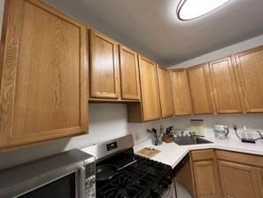 A kitchen with wooden cabinets, a stainless steel stove, and a microwave. - Charming Mid-Century Designed Apartment in Lakeview (Chicago)