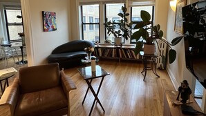 Una sala de estar con un sofá de cuero marrón, una mesa de centro de vidrio y una estantería.