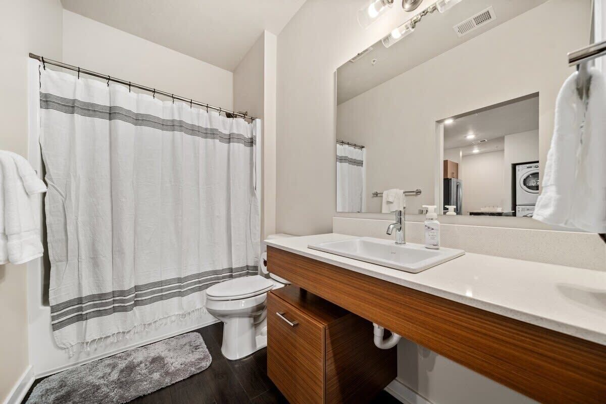Une salle de bain moderne avec un rideau de douche, des toilettes, un lavabo et un miroir.