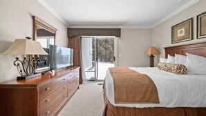 Una habitación de hotel con cama, televisor, cómoda y puerta corrediza al exterior.