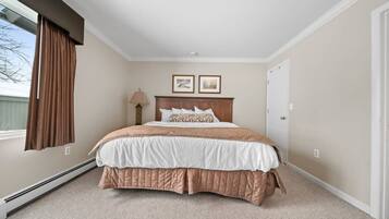 Un dormitorio con cama, ventana con cortinas, lámpara de pared y dos cuadros enmarcados.