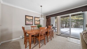 Un comedor con mesa y sillas de madera, una lámpara colgante y vistas a un paisaje nevado a través de grandes puertas corredizas de vidrio.