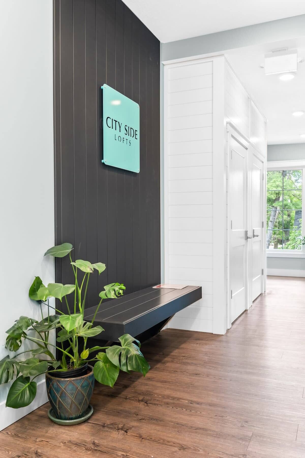 A modern interior with a dark wooden wall, a sign reading "CITY SIDE LOFTS," and a potted plant.