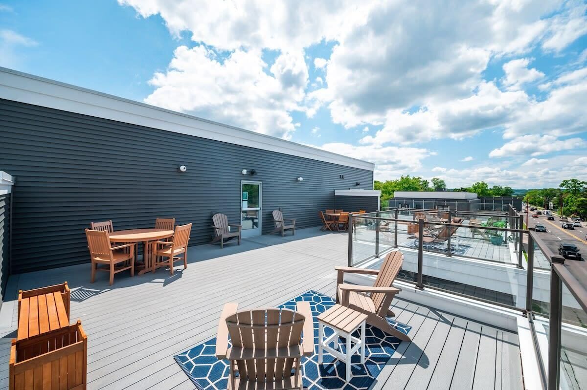A modern building with a flat roof deck featuring outdoor furniture and a glass railing overlooking a street.