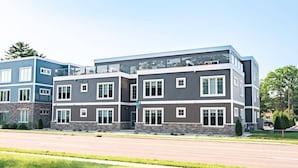 A modern multi-story residential building with a flat roof, large windows, and a mix of siding colors. - 2BR Condo | King Bed + Shared Rooftop + Dogs (Traverse City)