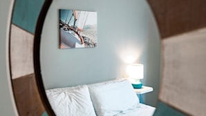 A circular mirror with a wooden frame, reflecting a bed with white linens and a nightstand with a lamp. - 2BR Condo | King Bed + Shared Rooftop + Dogs (Traverse City)