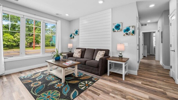 A modern living room with a sofa, coffee table, and side tables. There are large windows, a patterned rug, and artwork on the walls. - 2BR Condo | King Bed + Shared Rooftop + Dogs (Traverse City)