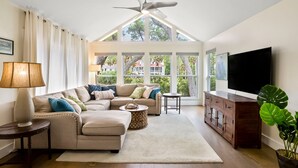 A living room with a large window, a ceiling fan, a sofa, a coffee table, a TV, and a cabinet. - **The Caddy's Shack** 1 story home with Club Cards Optional (Fripp Island)