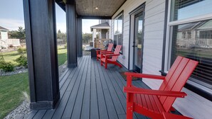 Una terrazza coperta con poltrone Adirondack rosse, pavimento in legno e vista su un quartiere residenziale.