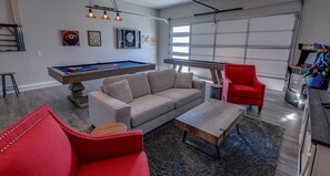 Un salon moderne avec une table de billard, un fauteuil rouge et un jeu de fléchettes.
