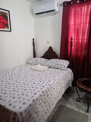 Ein Schlafzimmer mit einem Bett, einem roten Vorhang, einer Wand-Klimaanlage und einem gerahmten Bild an der Wand.