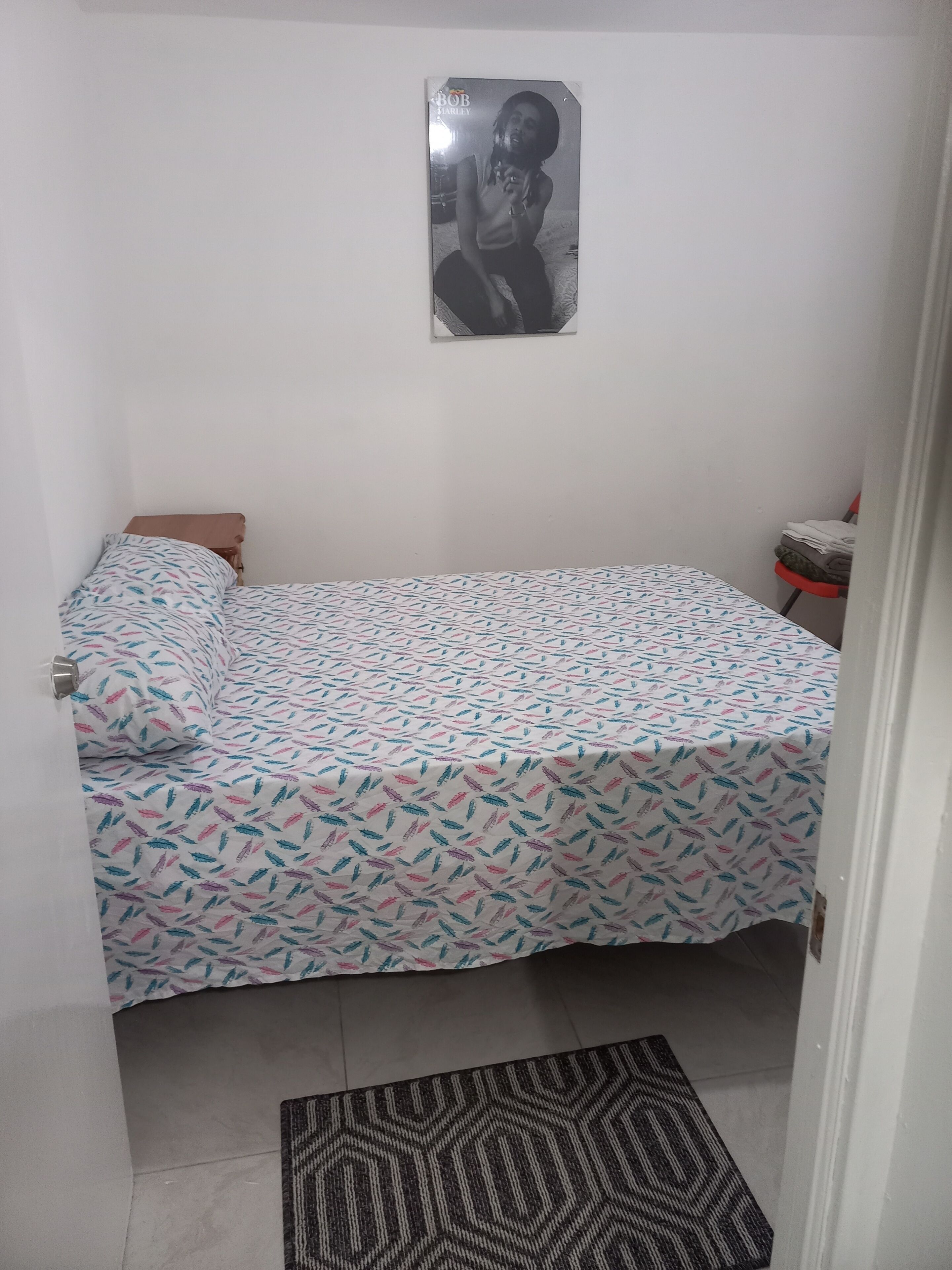 Una habitación pequeña con cama individual, una colcha estampada, un cuadro en la pared y una alfombra en el suelo.