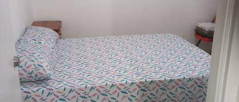 Una habitación pequeña con cama individual, una colcha estampada, un cuadro en la pared y una alfombra en el suelo.