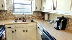 A kitchen with white cabinets, a stainless steel sink, a dishwasher, and a coffee maker on the countertop. - Cozy 3 bedroom house (Indianapolis)