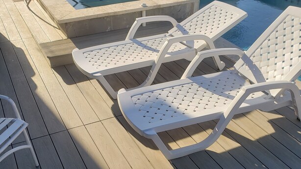 Una terraza de madera con piscina y sillones de descanso.