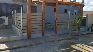 Un patio cubierto con listones de madera y una pérgola, una planta en maceta y una ventana con persianas.