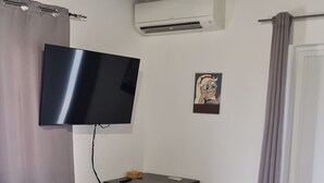 Una habitación con una televisión de pantalla plana en la pared, una mesita con dos sillas y un ventilador de techo.