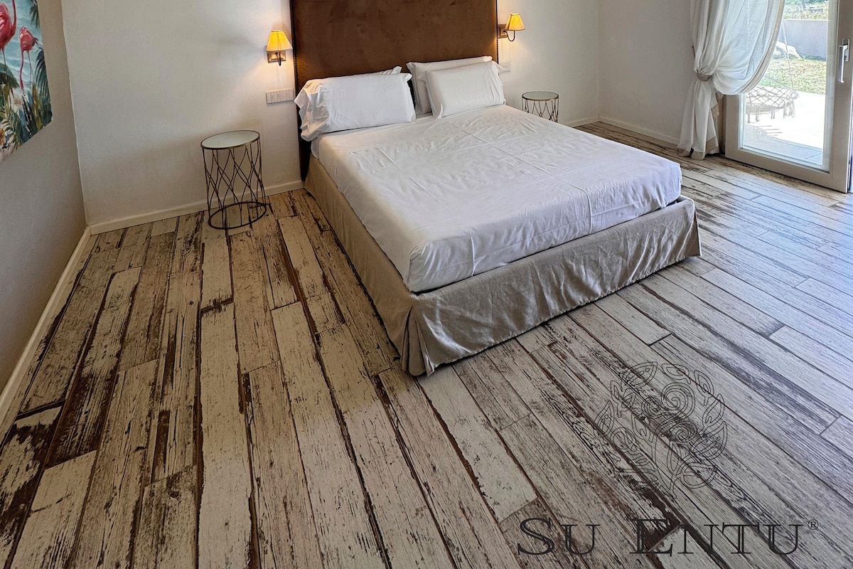 A bedroom with a wooden floor, a bed with white bedding, two bedside lamps, and a painting on the wall.