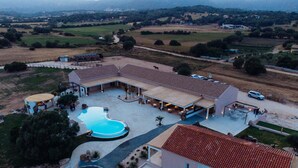 Vista aérea de una propiedad con piscina, zonas de estar al aire libre y un edificio grande con techo de tejas.