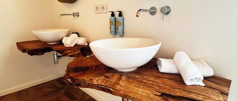 A bathroom with a wooden vanity, two large oval mirrors, a white vessel sink, and a wooden floor with a geometric pattern.