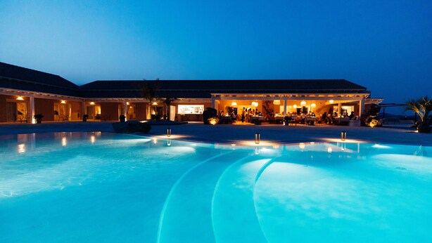 Un hotel con una piscina grande, zona de comedor al aire libre y varias habitaciones.