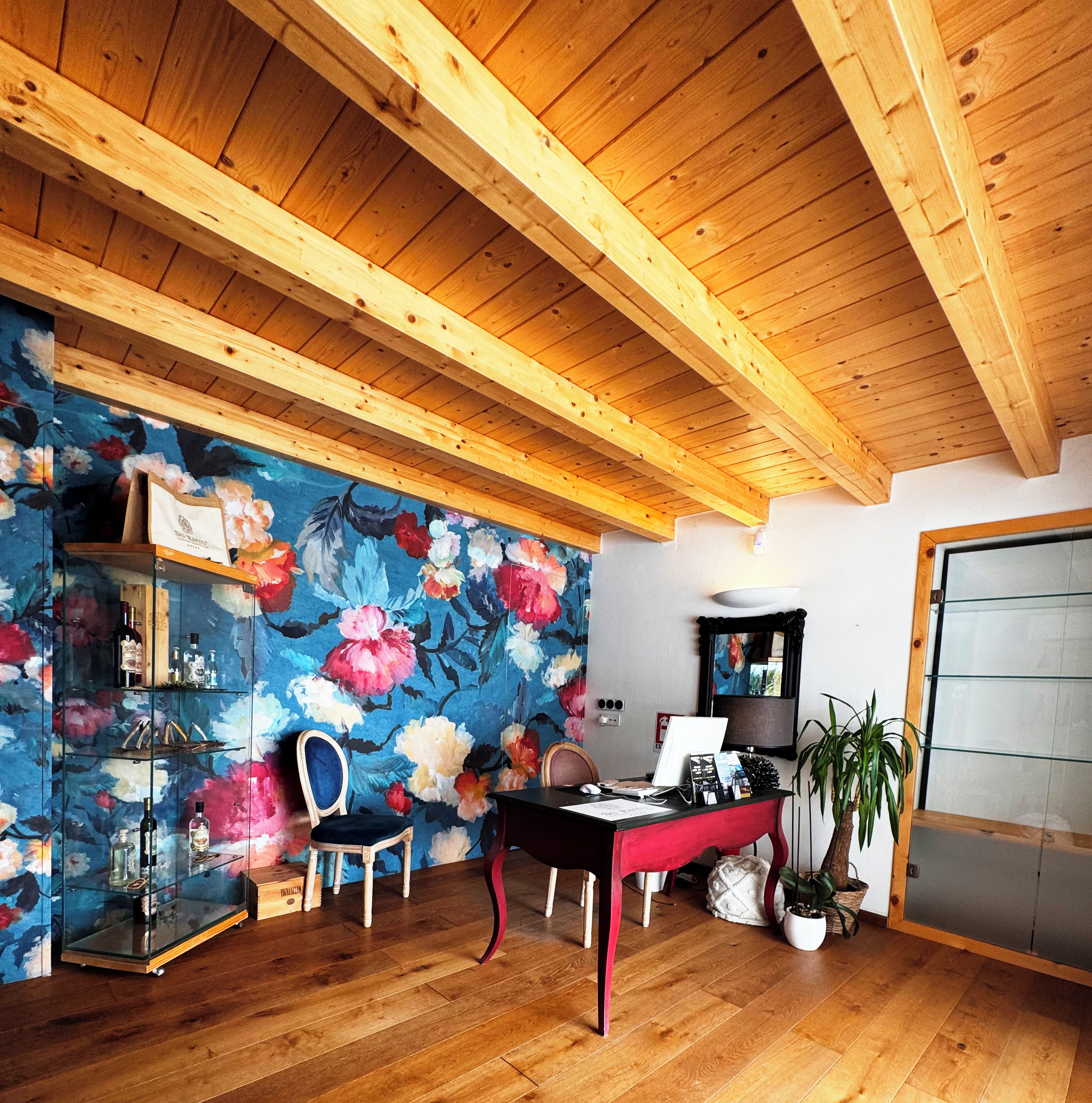 A room with wooden flooring, a desk, a chair, a glass cabinet, and a floral wall mural.