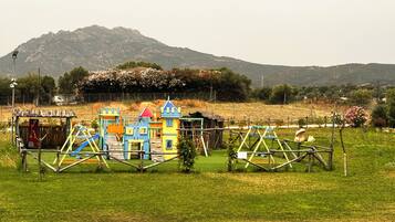A playground with colorful play structures in a grassy field with a mountain in the background.