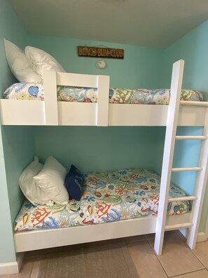 A bunk bed with a 'Beach Bum Club' sign above it, featuring a colorful bedspread with sea creatures.
