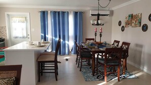 Un comedor con una isla central, sillas de madera, un tapete estampado y una mesa de comedor con platos y tazas.