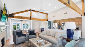 A spacious living room with a fireplace, a large window, and a kitchen area with wooden cabinets. - Wayfarer cottage with elevator and Heated pool! (St Simons Island)