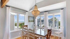 A dining area with a glass table, white chairs, and a hanging chandelier. - Wayfarer cottage with elevator and Heated pool! (St Simons Island)