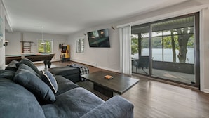 Una sala de estar moderna con mesa de billar, asientos cómodos y un amplio ventanal corredizo que da a un balcón con vistas a un lago.
