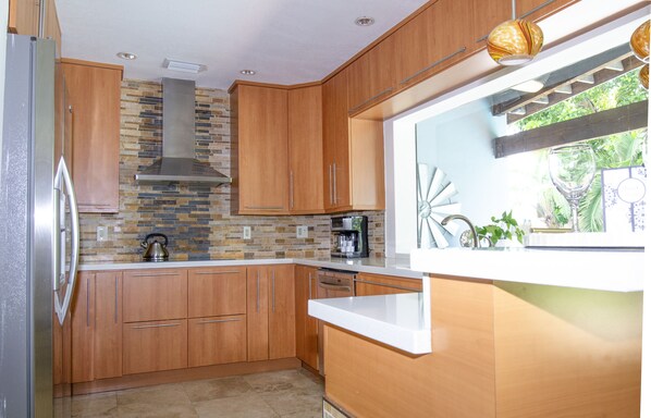 Une cuisine moderne avec des meubles en bois, un réfrigérateur en acier inoxydable, une cuisinière encastrée et une fenêtre donnant sur un paysage verdoyant.