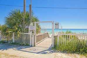 A gated beach entrance with a clear view of the ocean and beach umbrellas.