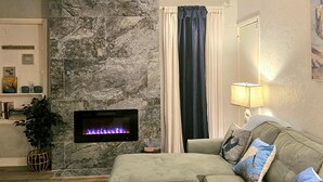 Ein Wohnzimmer mit Kamin aus Stein, einem grünen Sofa, einer Lampe und einem Fenster mit Vorhängen.