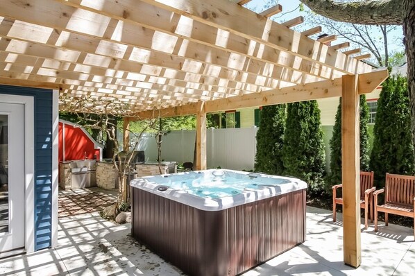 Ein Whirlpool unter einer Holzpergola in einem Garten mit Grillplatz und einer Holzbank.