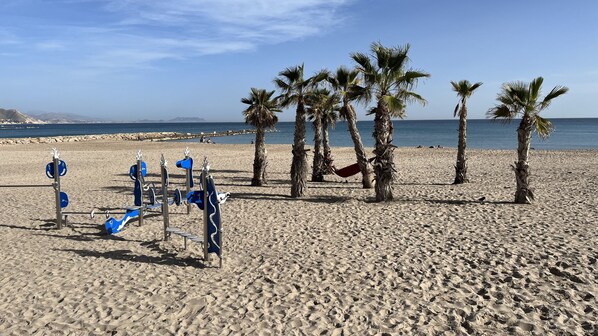 A sandy beach with palm trees and a row of blue exercise equipment.