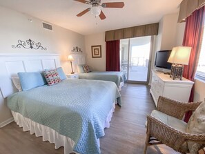 Ein Hotelzimmer mit zwei Betten, einem Deckenventilator, einem Fernseher, einem Korbstuhl und einem Balkon mit Blick.