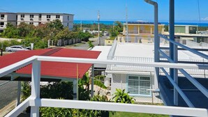 A view from a balcony overlooking a residential area with a clear blue sky, a body of water, and a distant shoreline.