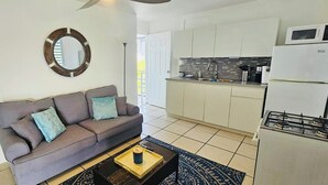 A living room with a grey sofa, a coffee table, and a kitchen area with white cabinets and a microwave.