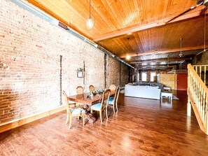 Cozy seating area with a dining table and sofa, surrounded by exposed beams and a brick wall.