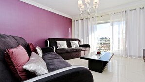 Un salon moderne avec un mur violet, deux canapés noirs avec des coussins blancs, une table basse noire et un lustre.