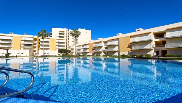 Une piscine à l’eau d’un bleu cristallin, entourée d’immeubles à plusieurs étages dotés de balcons.